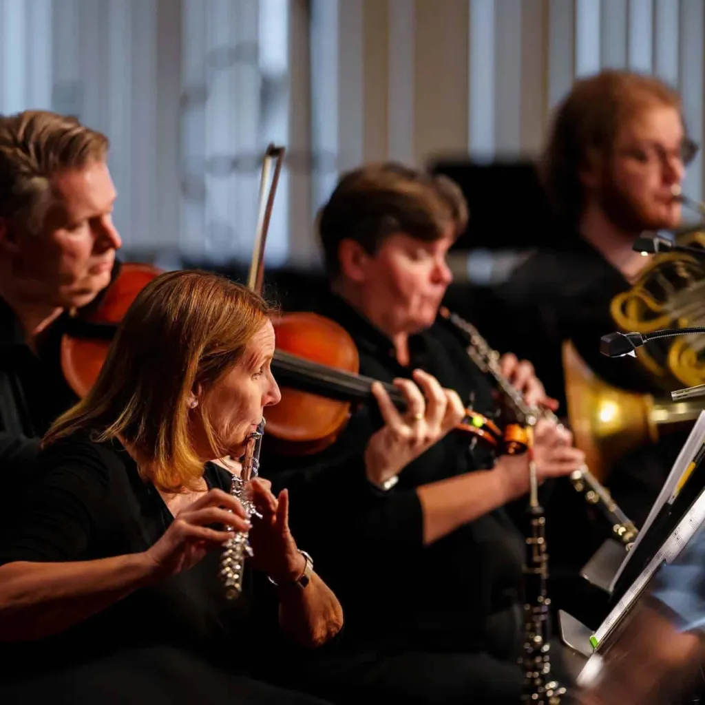Musicians play various instruments, including a flute, violin, and horn, during a performance.