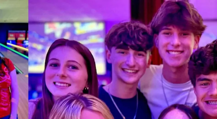 A group of young people smiles together at a bowling alley, with colorful lights and bowling lanes in the background.