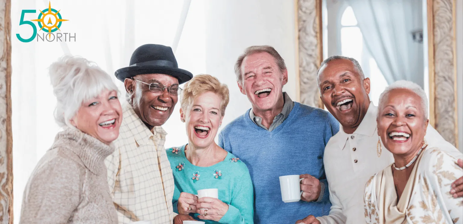 A group of six smiling seniors holds cups and poses together in a bright, airy room with mirrors.