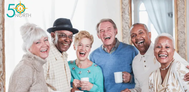 A group of six smiling seniors holds cups and poses together in a bright, airy room with mirrors.