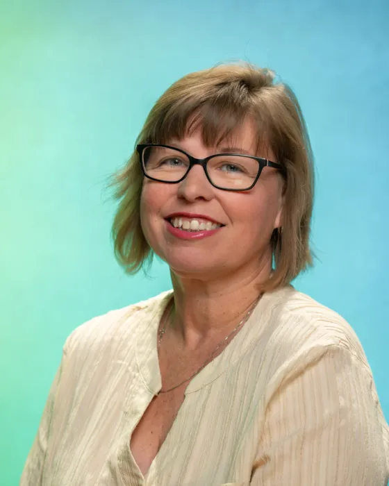 A woman with glasses smiles while posing against a gradient blue and green background.