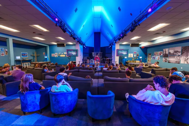Youth are seated on couches in a modern room, listening to a speaker at the front.