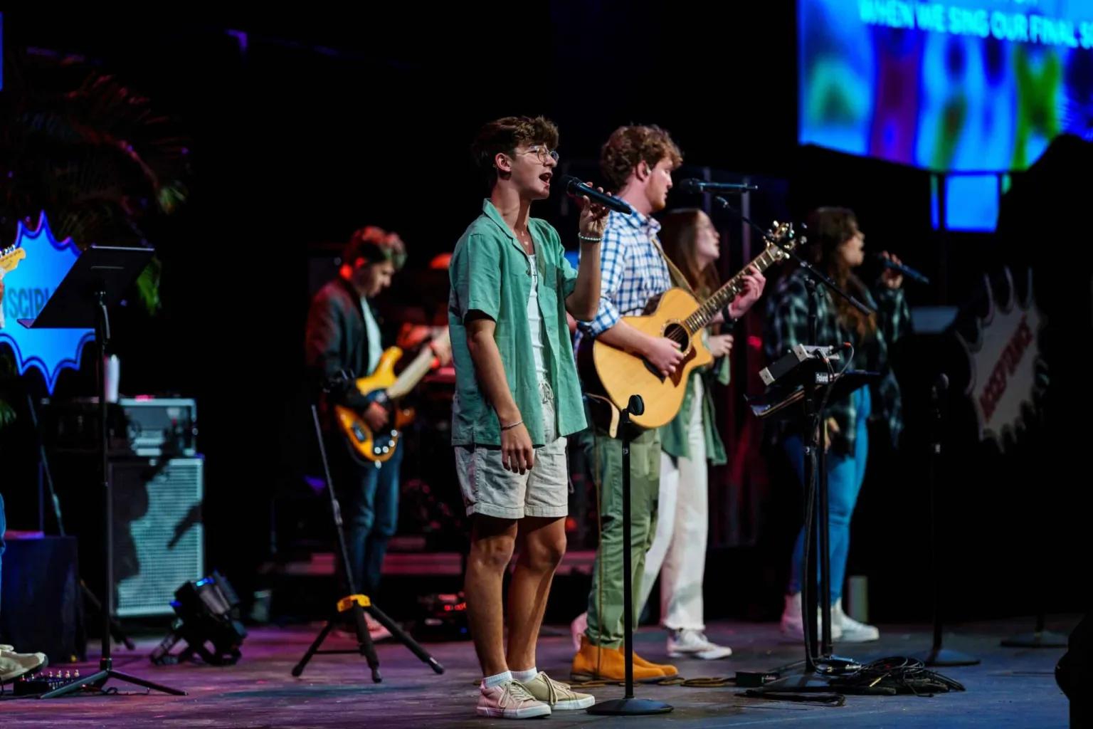 A youth choir performs on stage with microphones and instruments during a worship service.