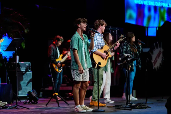 A youth choir performs on stage with microphones and instruments during a worship service.