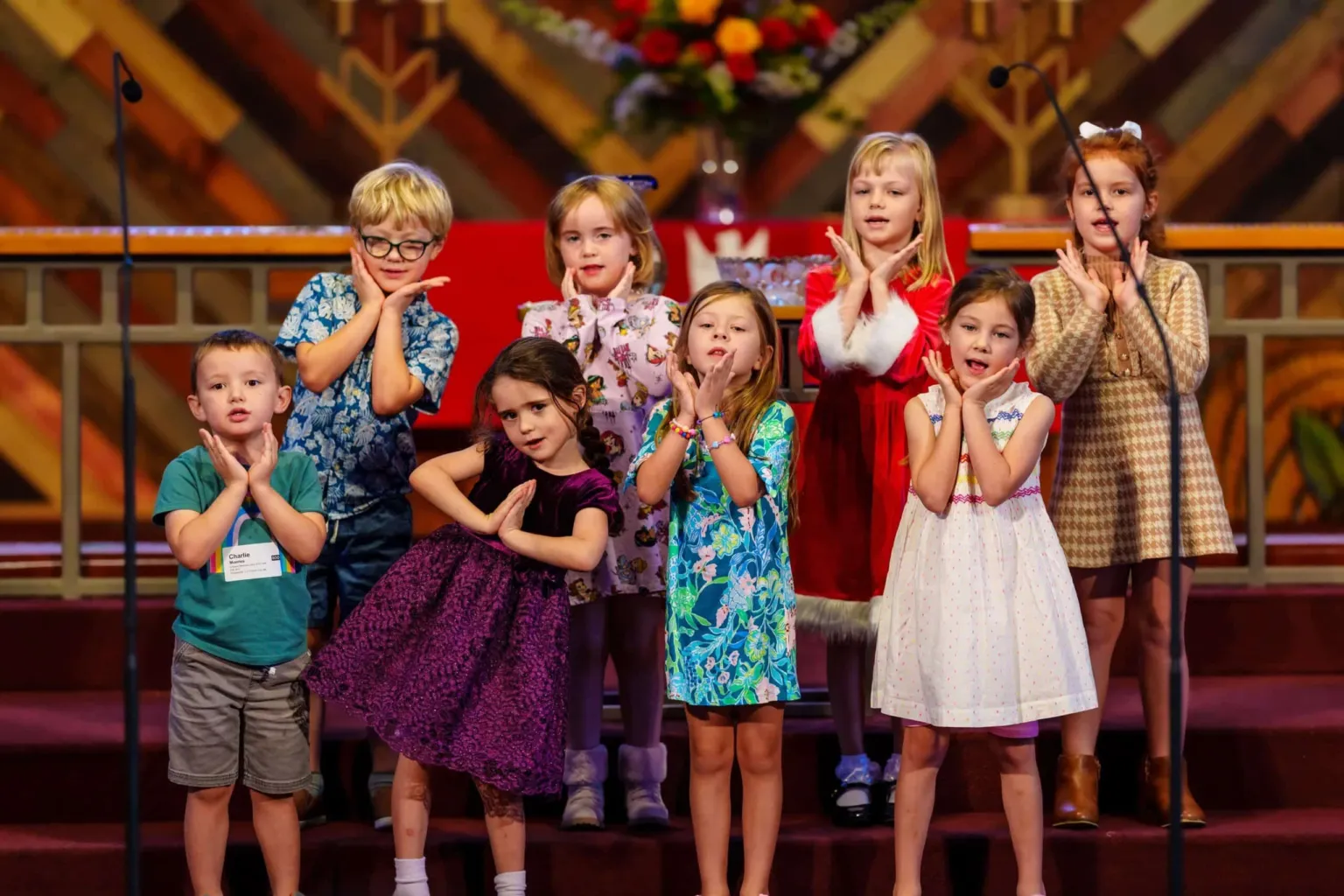 Children perform on stage, posing with playful expressions and gestures, dressed in colorful outfits.