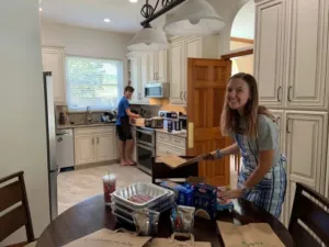 Two people are preparing food in a kitchen, with one smiling and the other focused on cooking.