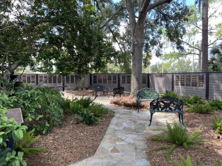 A memorial garden features benches and plaques along a stone pathway surrounded by greenery and trees.