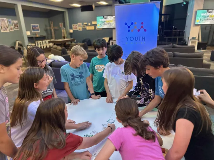 Youth group members gather around a table, collaborating on a creative project in a church setting.