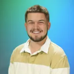 A young man with a beard smiles while wearing a striped shirt against a blue-green background.