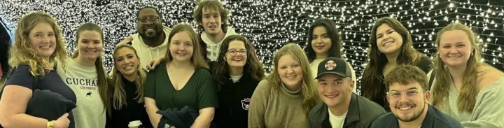 A group of young adults poses together in front of a backdrop of twinkling lights.