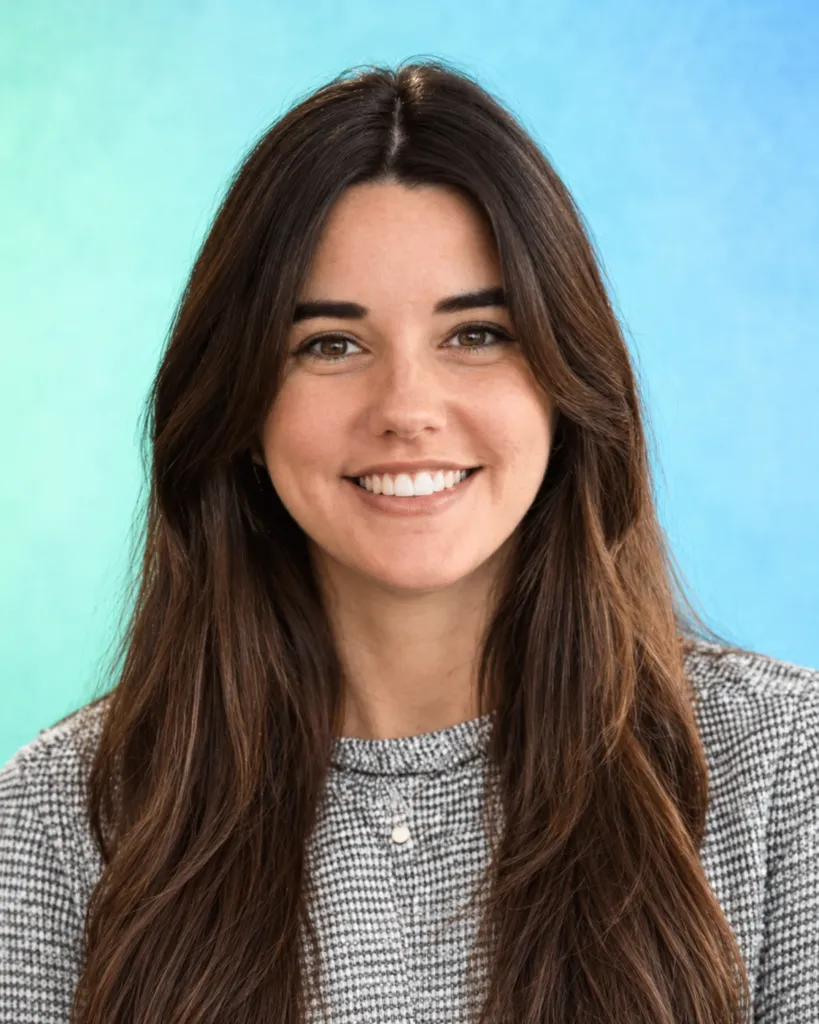 A woman with long dark hair smiles at the camera against a soft blue background.