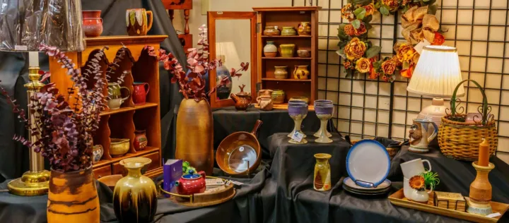 A display of various pottery, vases, and decorative items arranged on black fabric with a floral wreath in the background.