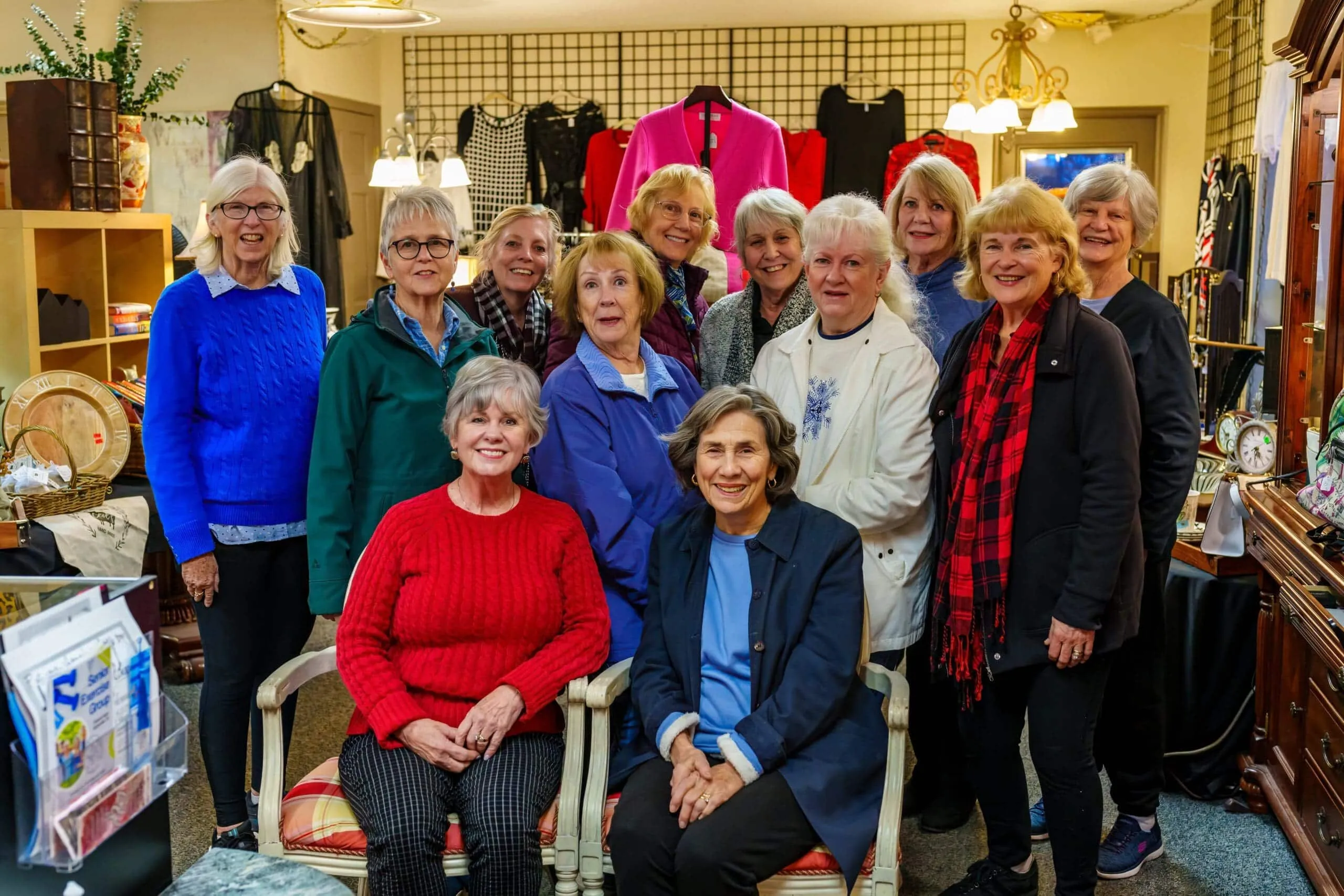 A group of twelve women poses together in a gift shop, surrounded by clothing and decorative items.
