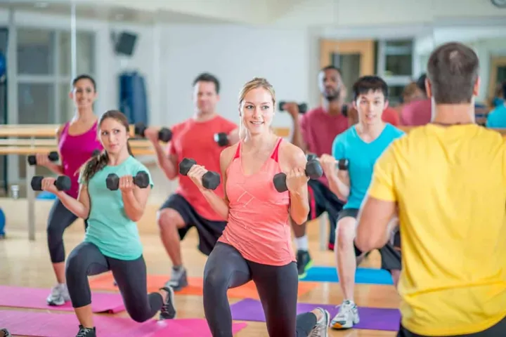 Participants are engaged in a group workout session, lifting dumbbells while following an instructor.