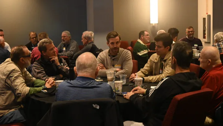 Men are seated around tables, engaged in conversation during a monthly breakfast event.