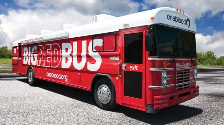 A red blood donation bus with "BIG RED BUS" and "oneblood.org" displayed on its side is parked outdoors.
