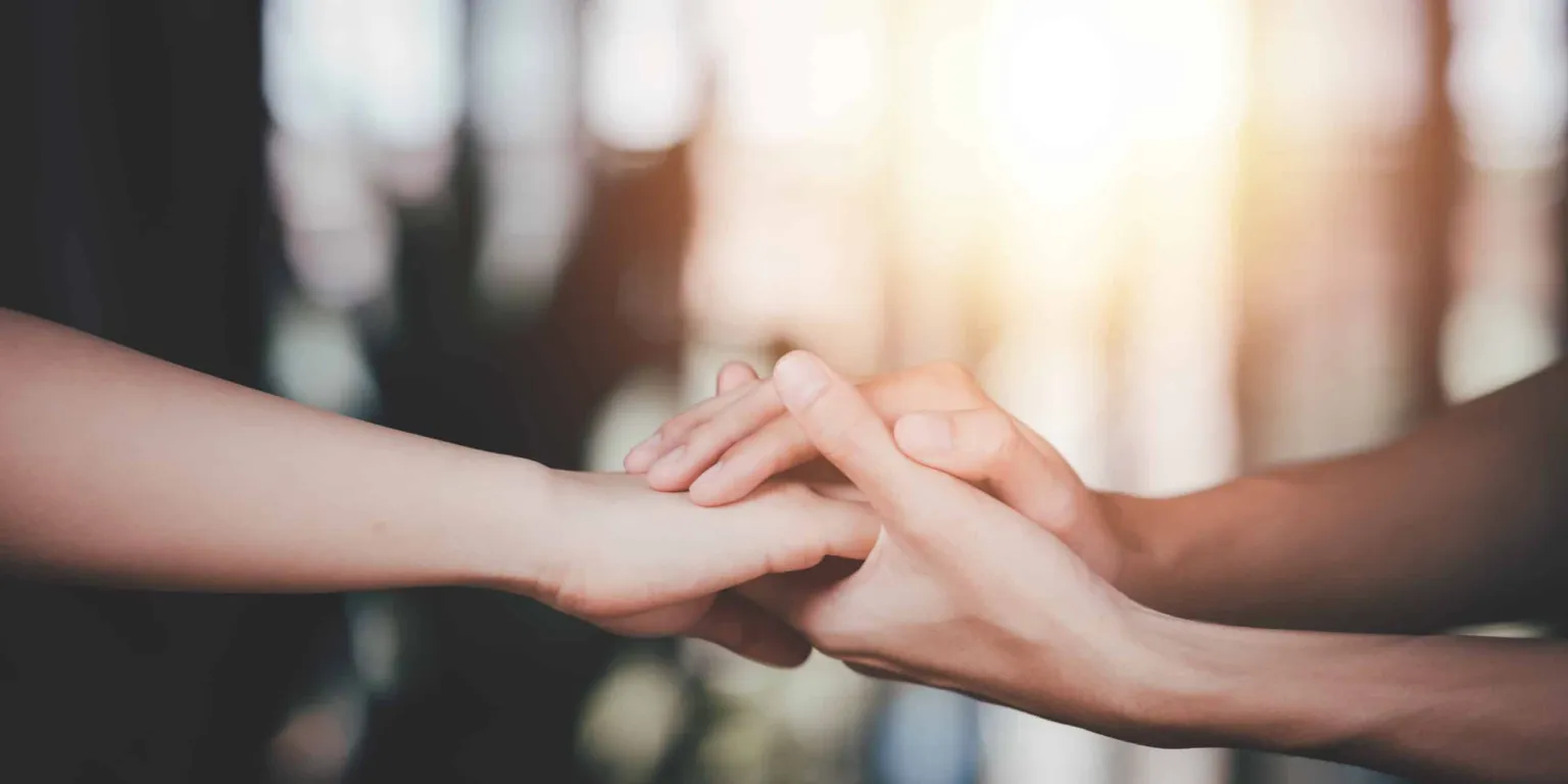 Two hands are gently clasping each other in a warm gesture of connection.