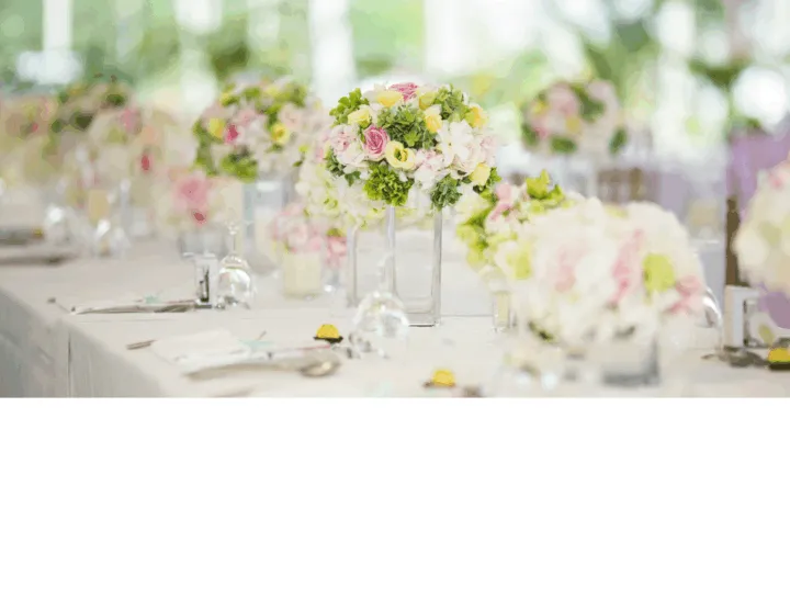 Table set for an event, adorned with clear vases of colorful flowers and neatly arranged place settings.