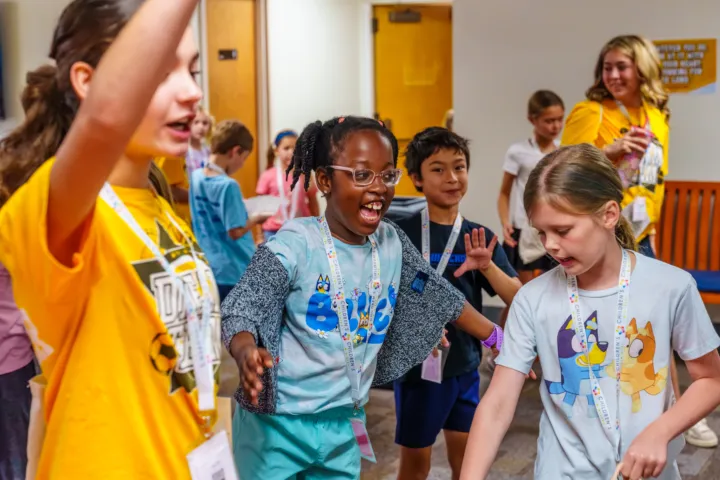 Children and teens are dancing and interacting in a hallway during a church event.