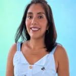 A woman smiles while wearing a light blue dress with buttons and embroidered designs, set against a gradient background.