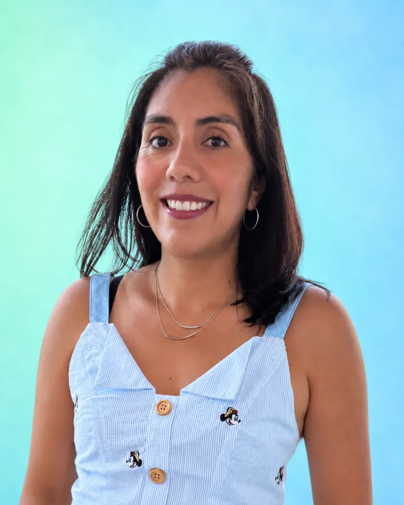 A woman smiles while wearing a light blue dress with buttons and embroidered designs, set against a gradient background.
